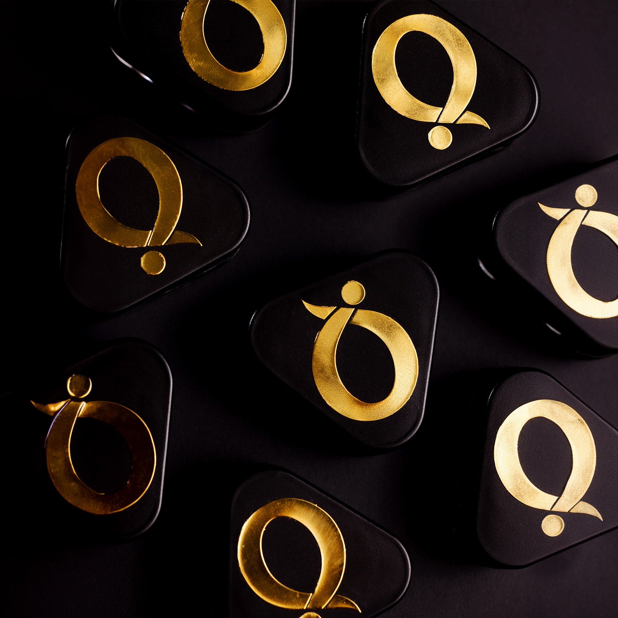 Several black, triangular boxes with bold, shiny gold abstract symbols on the lids are arranged on a dark background, creating a luxurious and modern appearance.