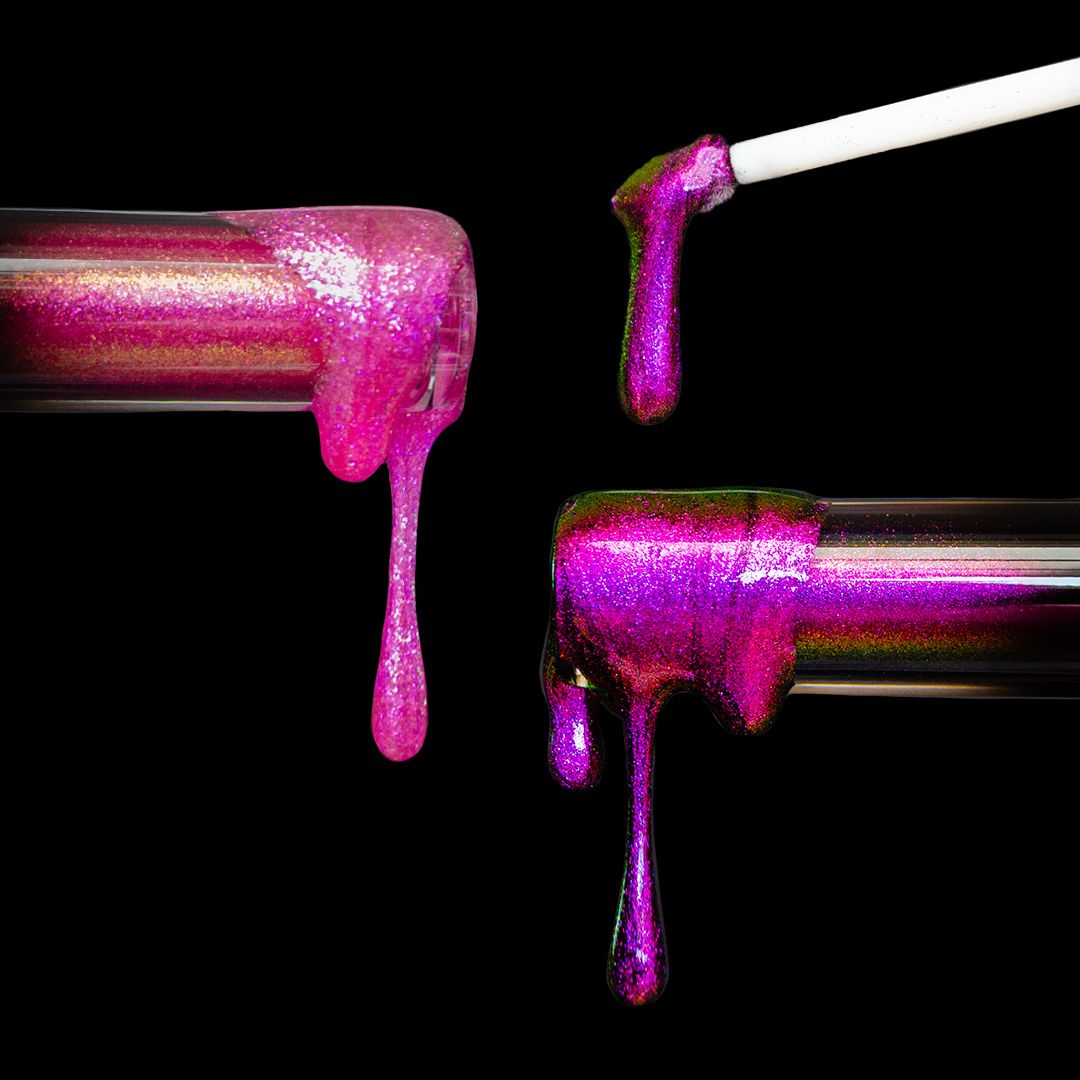 Shimmery, pink-purple nail polish drips from two glass bottles and a brush against a black background.