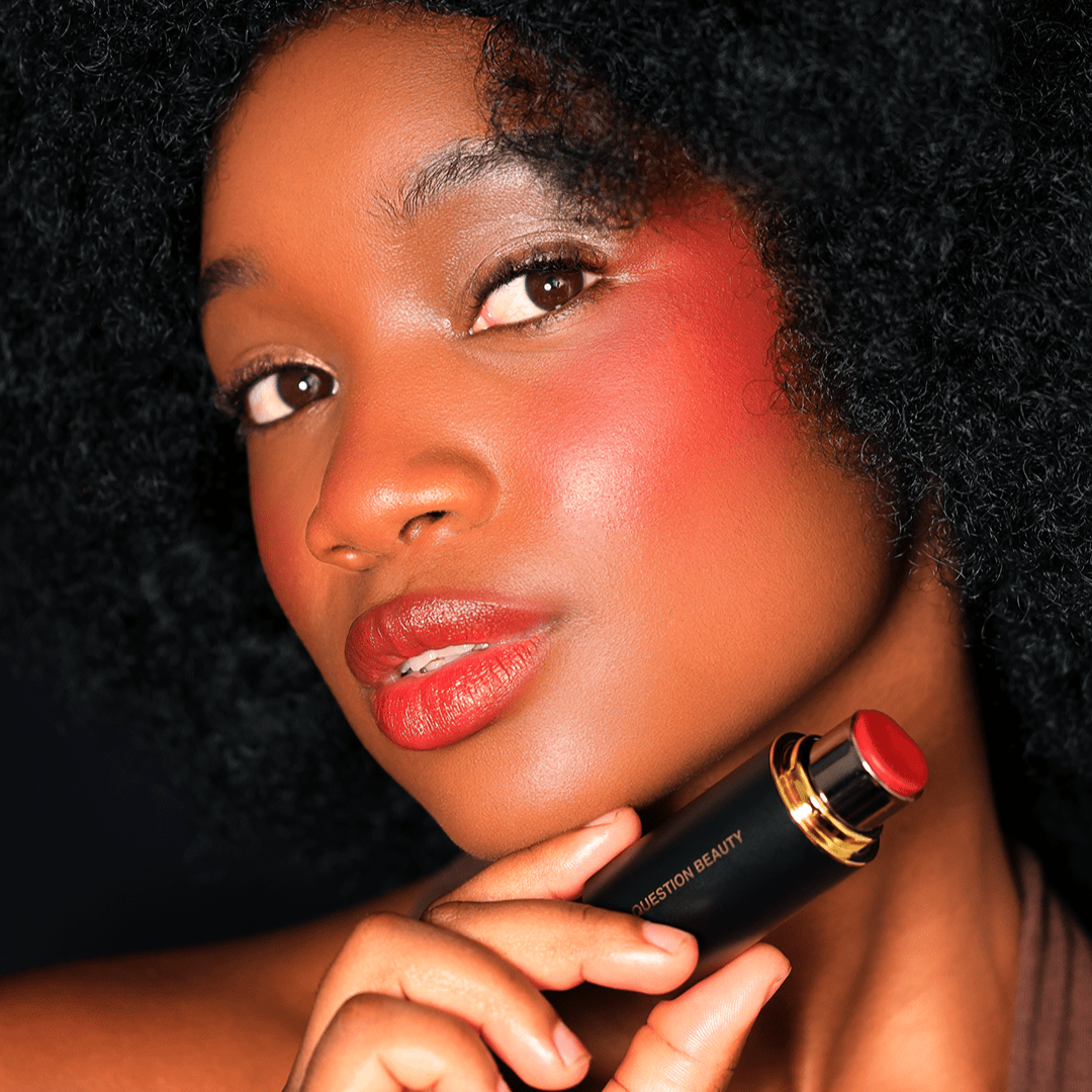 A woman applies red blush to her cheek