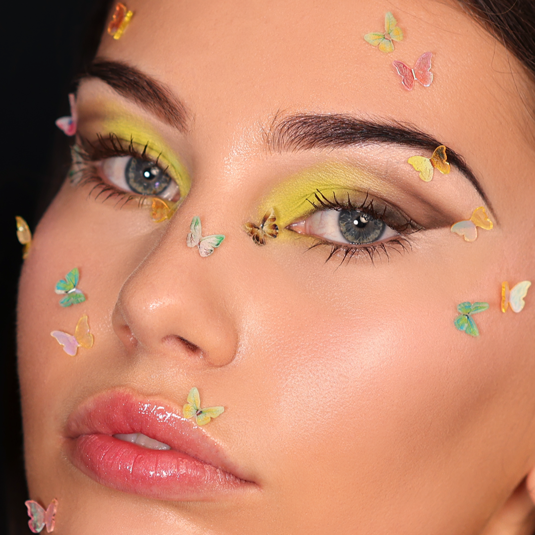 Woman with bright green eyeshadow and butterfly-shaped gems looks directly at the camera.
