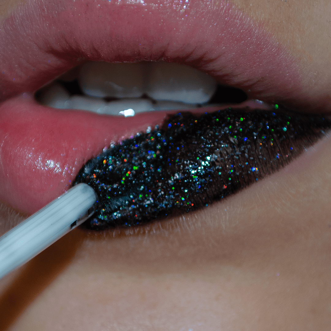 Close-up of lips with shimmering dark lip gloss being applied using a brush applicator.
