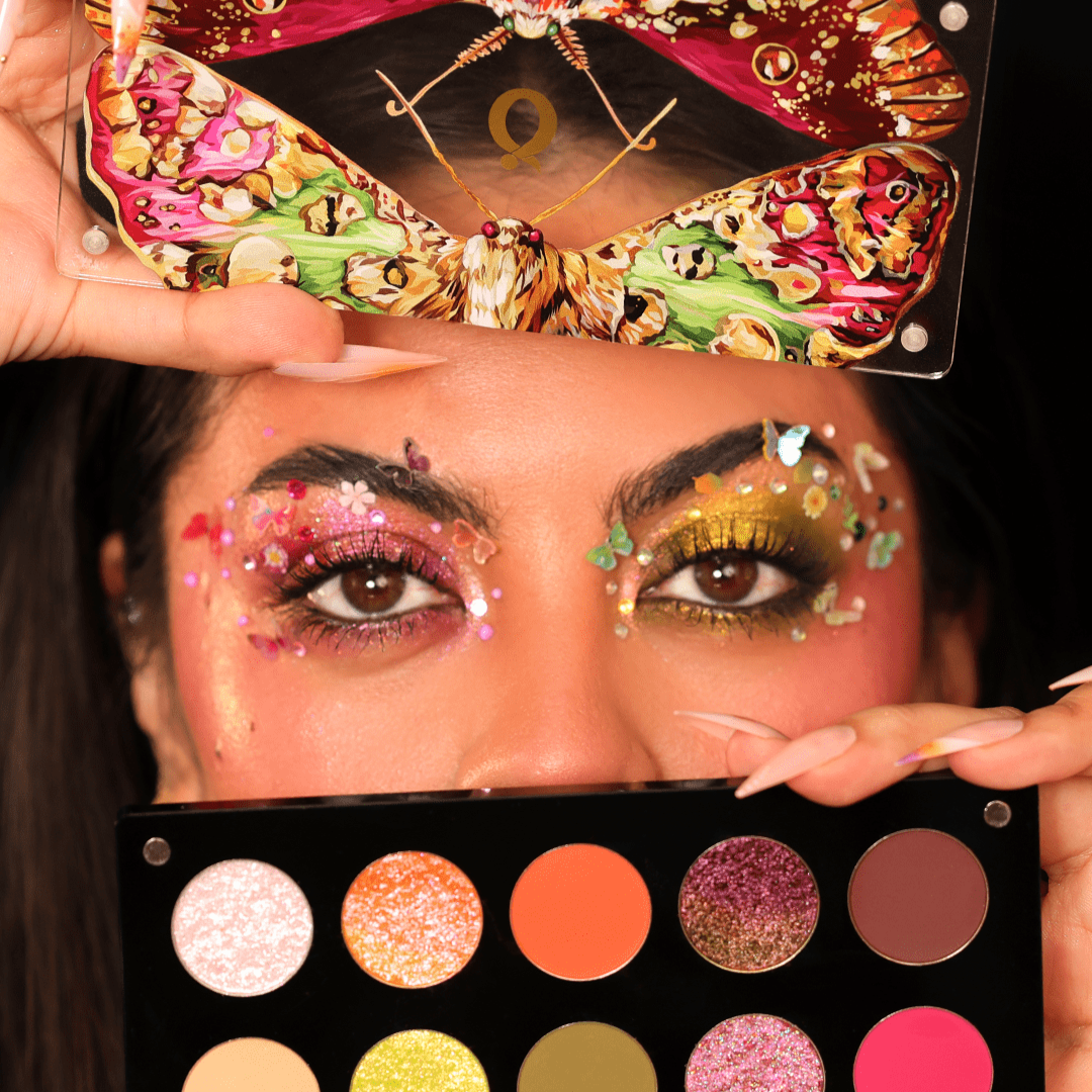 A person with vibrant eye makeup holds a palette and a moth-patterned lid.