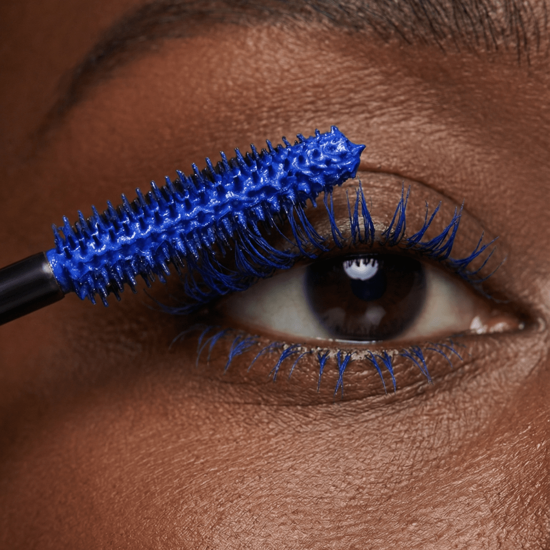 Close-up of an eye with blue mascara being applied to the upper and lower lashes using a wand.