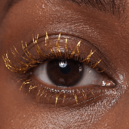 Close-up of a brown eye with gold lashes wearing Mascara Topper Sunlit Treasure.