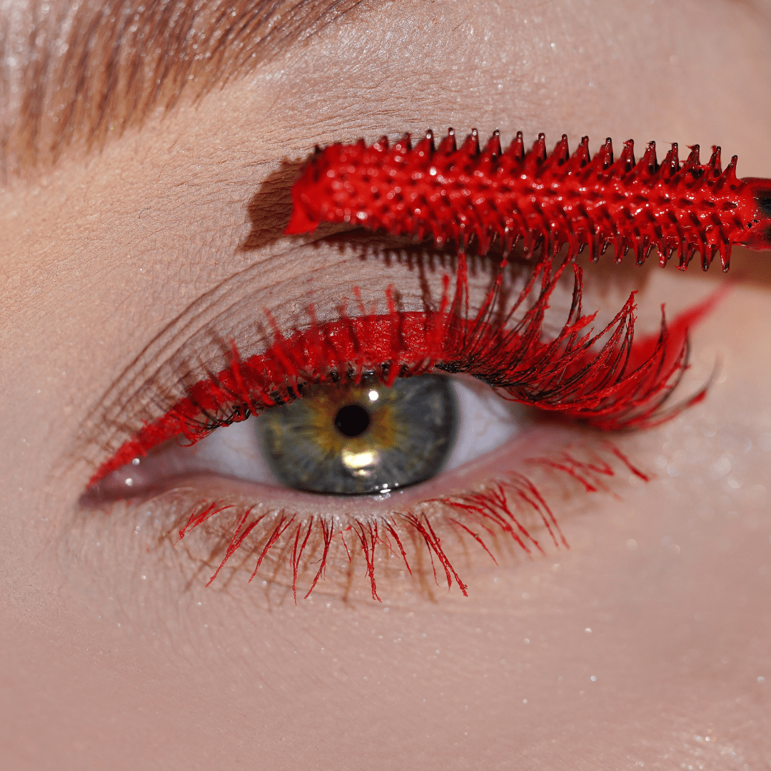 Close-up of an eye with red mascara being applied to the upper lashes.