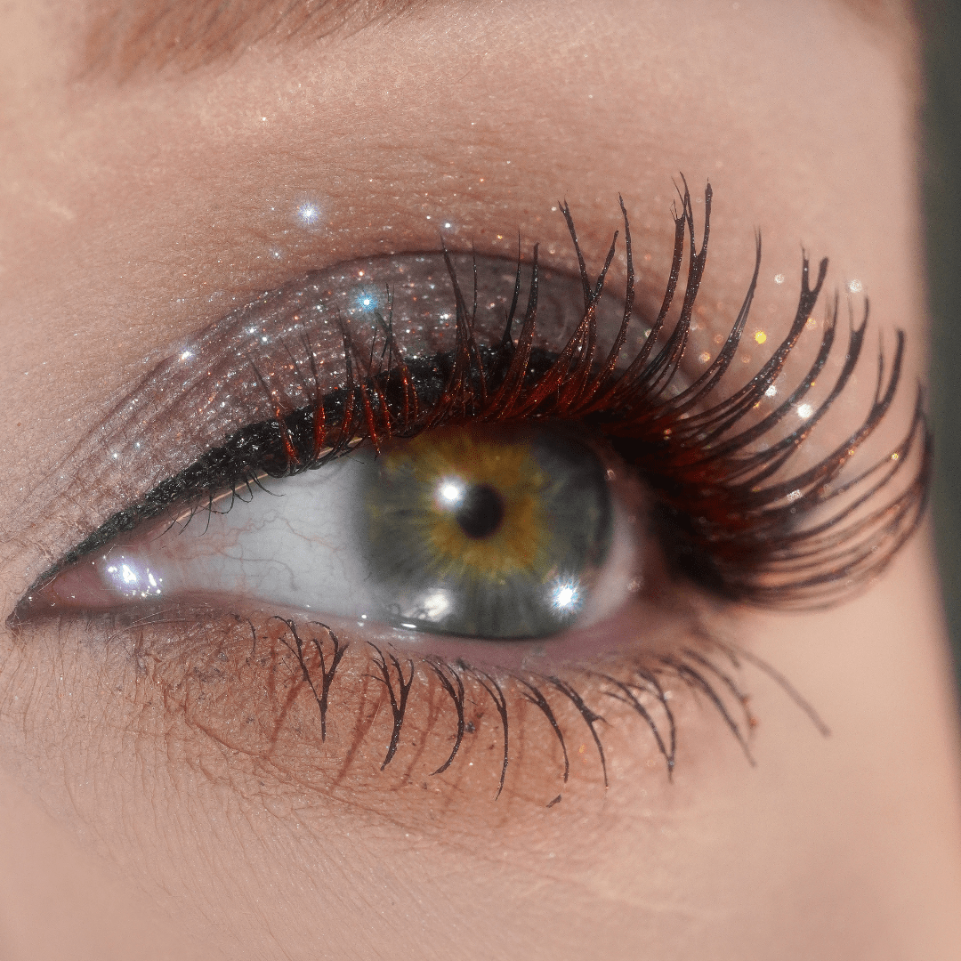 Close-up of an eye with glittery eyeshadow, thick black liner, and long lashes topped with dark red
