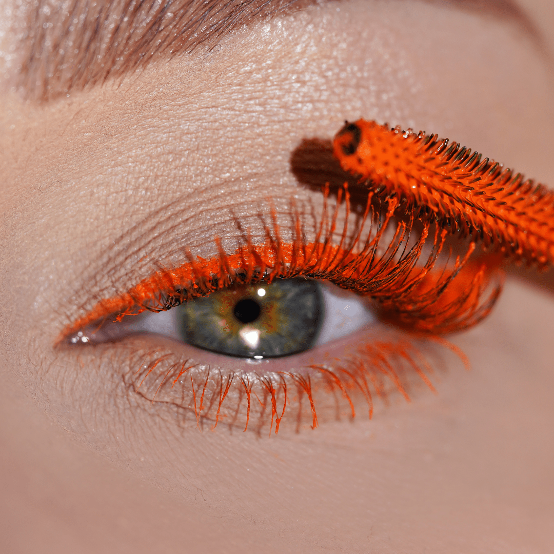 Close-up of an eye with orange mascara applied to upper and lower lashes