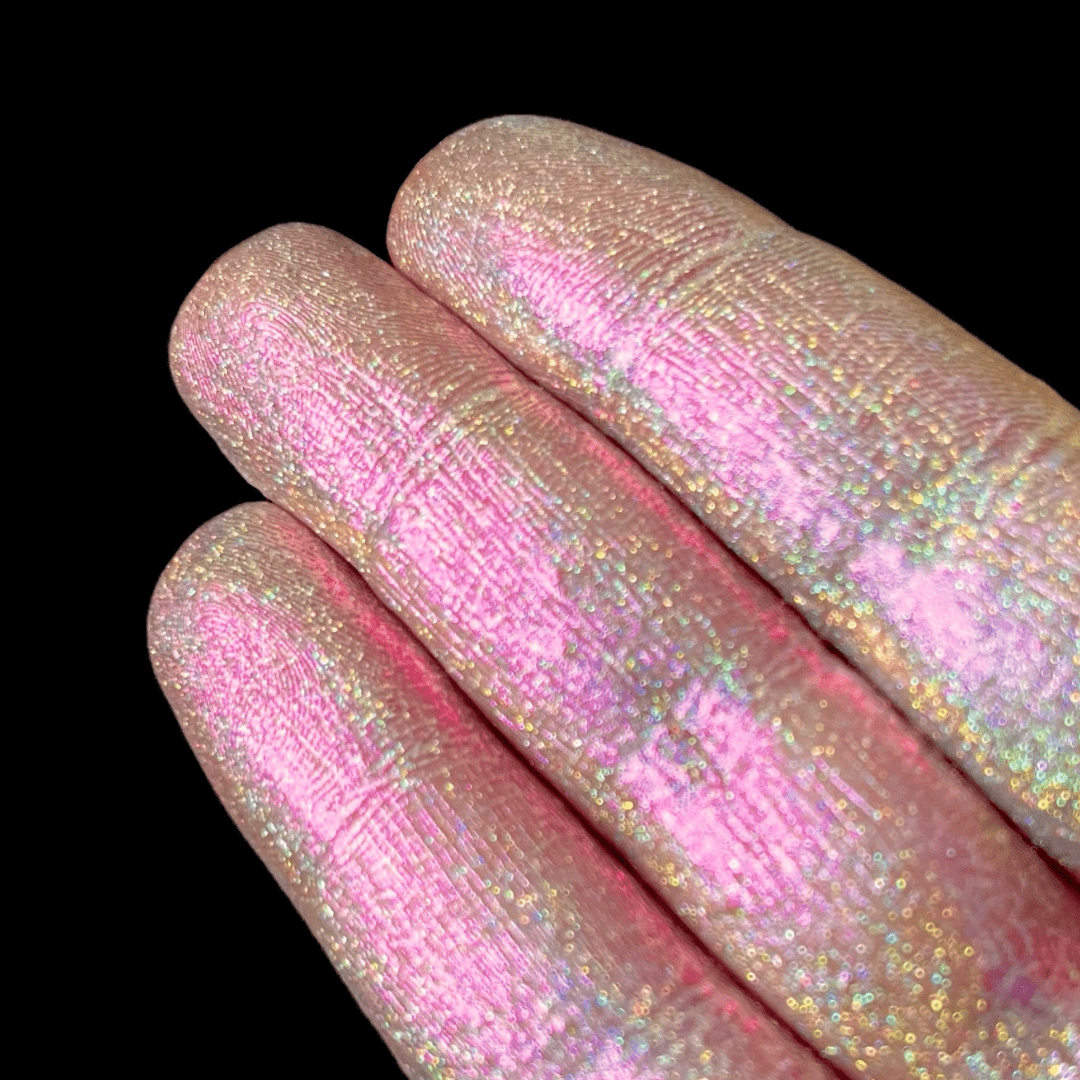 Three fingers covered in shimmery pink and gold glitter are shown against a solid black background.