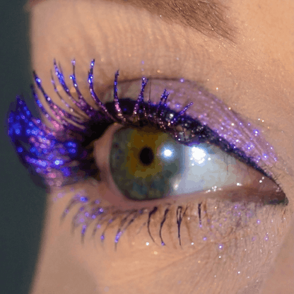 Close-up of an eye with glittery purple eyeshadow and thick black lashes.