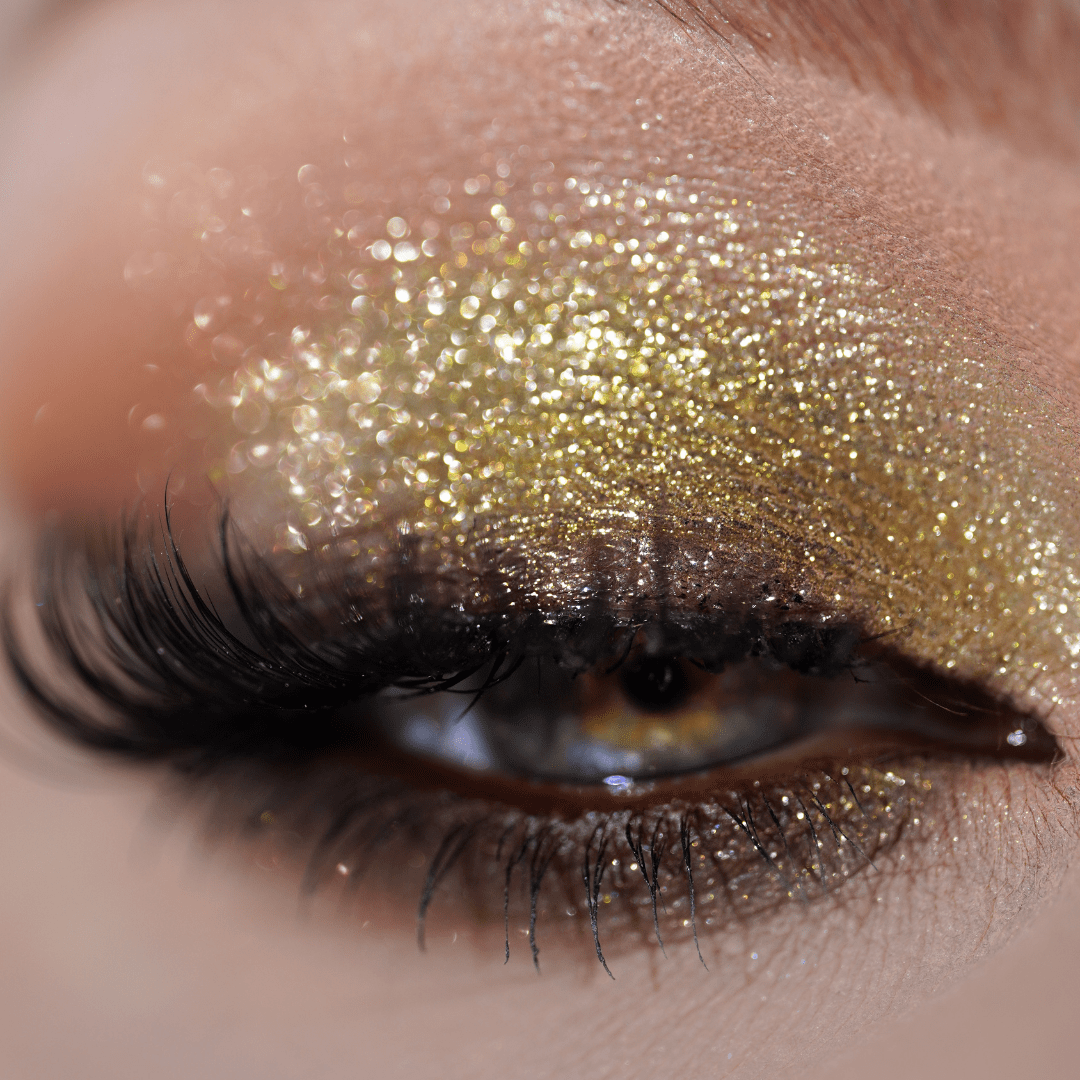 Close-up of an eye with gold glitter eyeshadow and long black lashes.