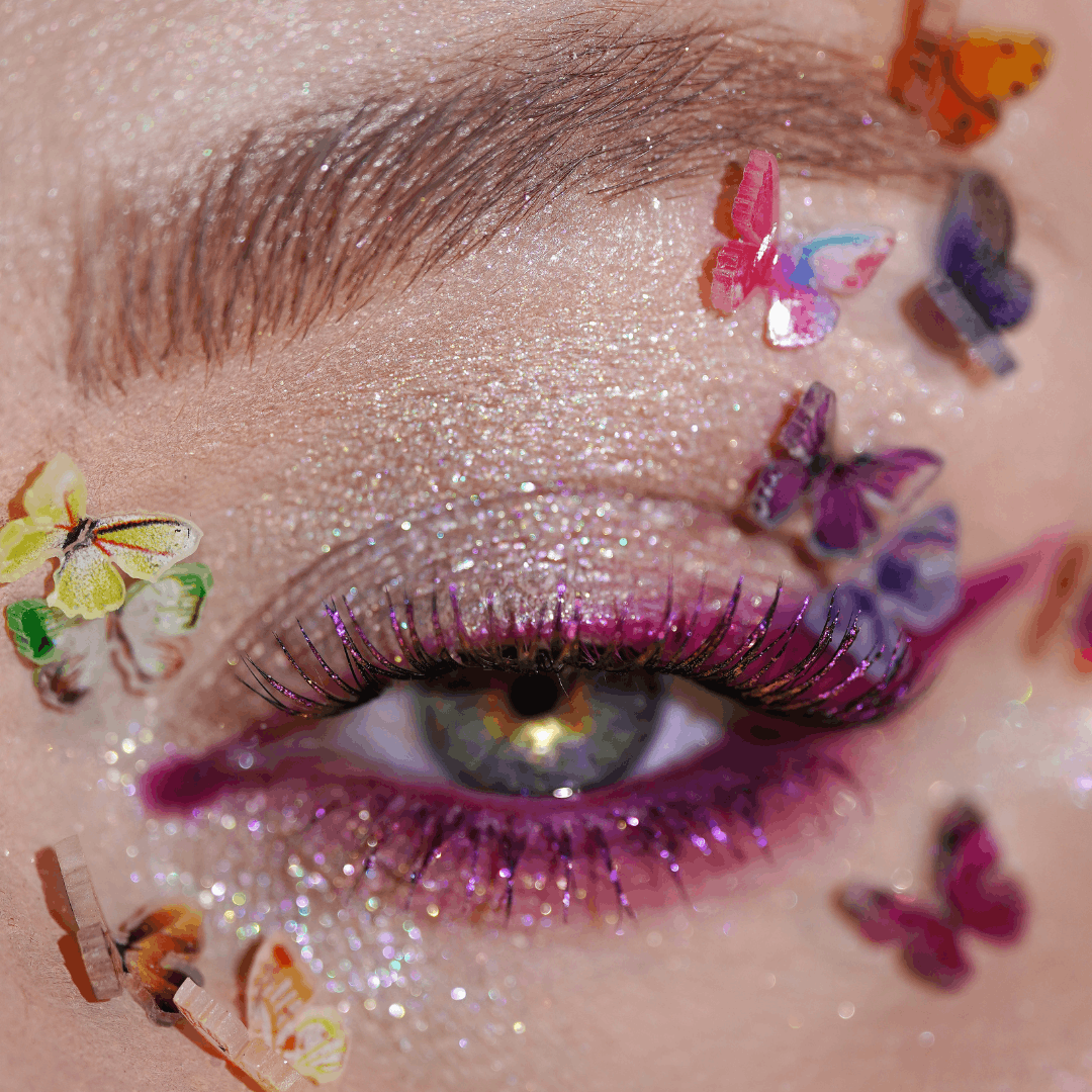 Close-up of an eye with glittery makeup, purple eyeliner, and colorful butterfly decorations and gems around the eye.