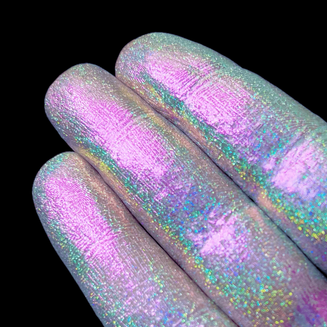 Three fingers display iridescent pastel pigment on their nails against a solid black background.