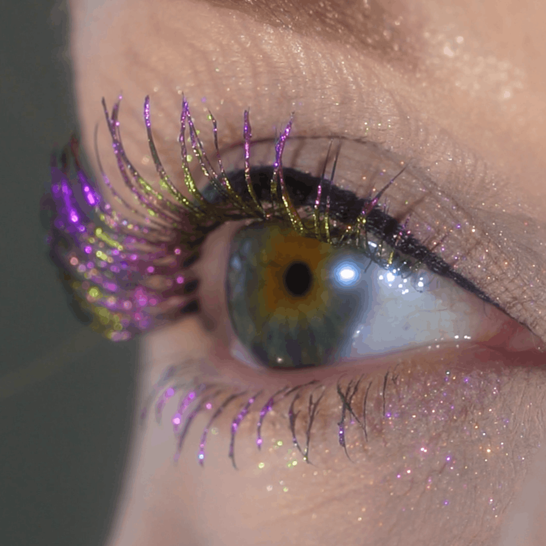 Close-up of an eye with gold and purple glitter mascara and shimmery eyeshadow on the eyelid.
