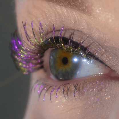 Close-up of an eye with gold and purple glitter mascara and shimmery eyeshadow on the eyelid.