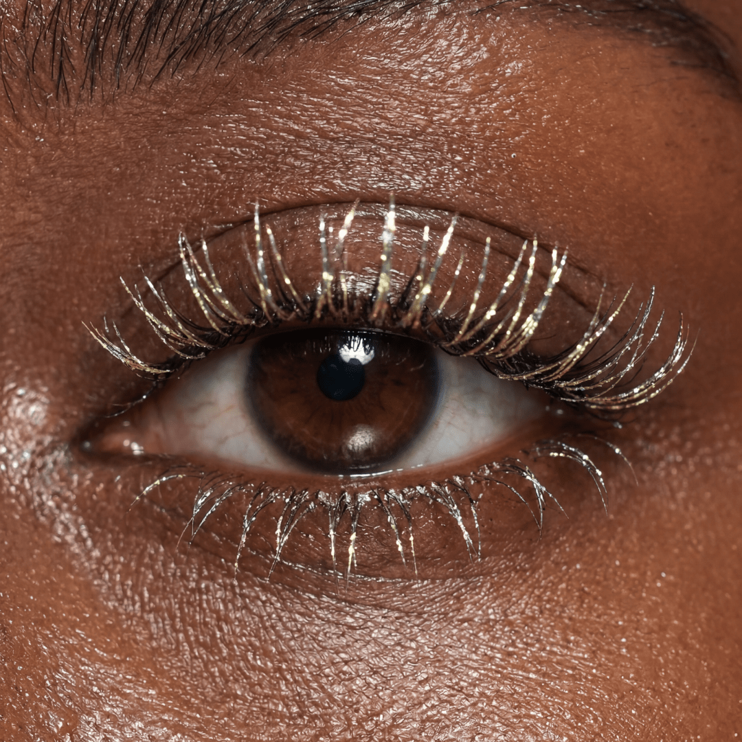 Close-up of a brown eye with silver mascara on the upper and lower lashes.