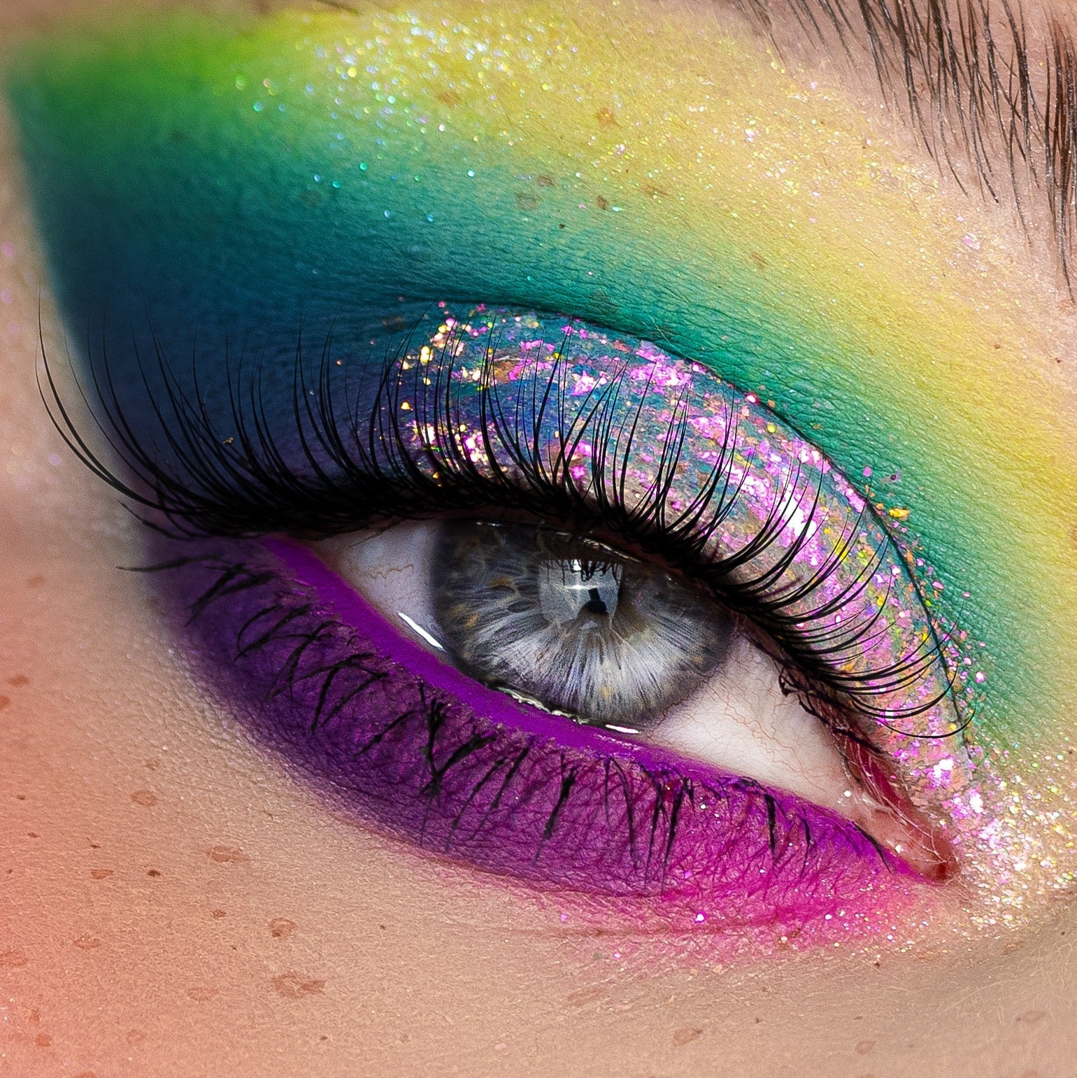Close-up of an eye wearing multicolored eyeshadow in blue, yellow, purple, and pink with sparkling glitter accents.