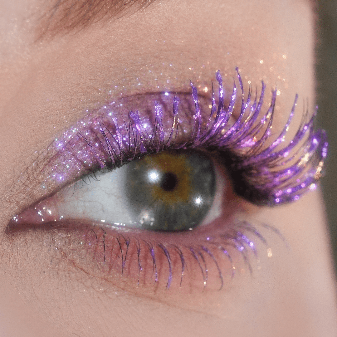 Close-up of an eye with pink shimmering mascara and matching pink glitter makeup around the eyelid.
