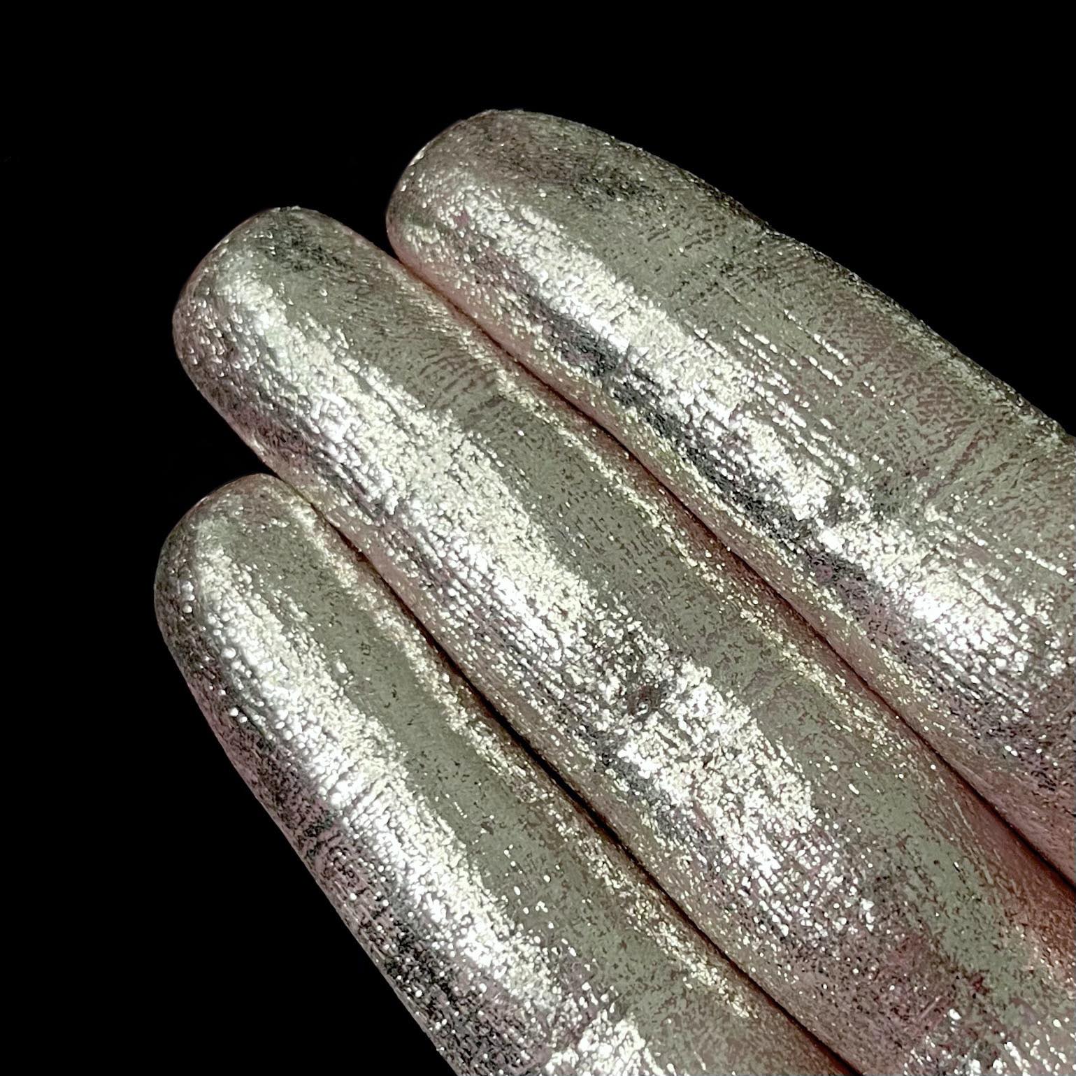 Three fingers display metallic silver pigment against a solid black background.