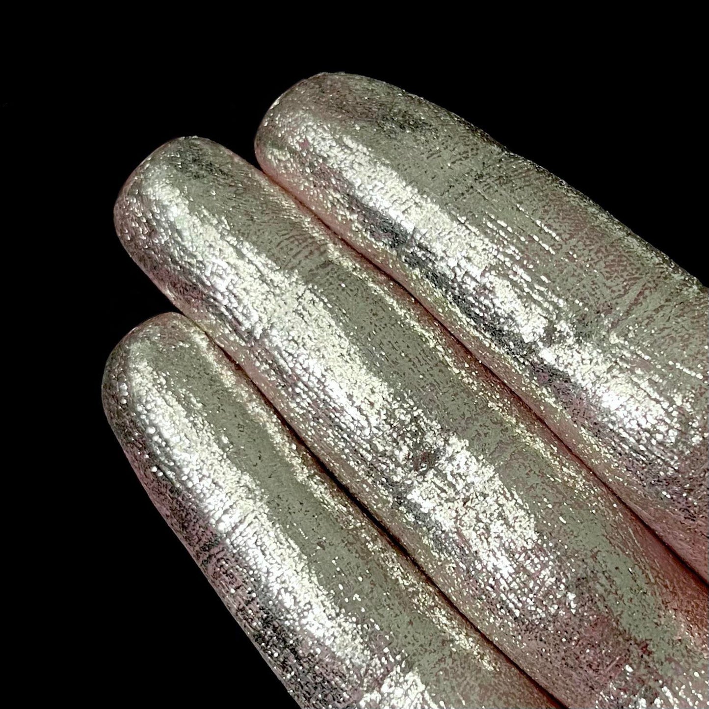 Three fingers display metallic silver pigment against a solid black background.