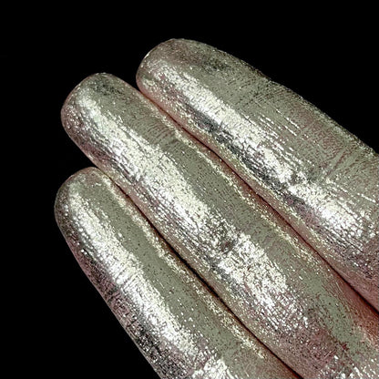 Three fingers display metallic silver pigment against a solid black background.