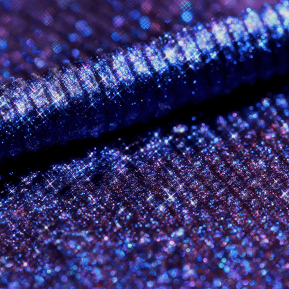 Close-up of a mascara topper in iridescent purple-blue with holographic glitter and a ribbed texture.