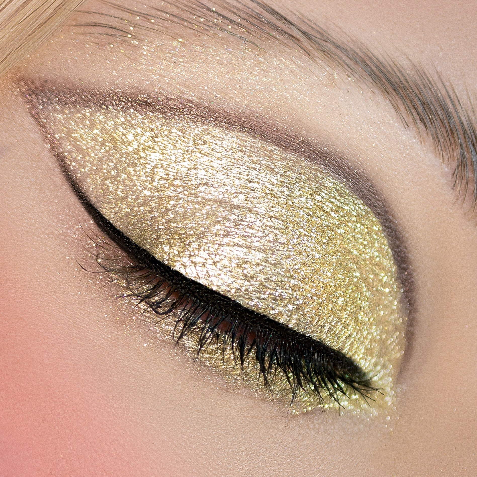 A closed eye with gold glitter eyeshadow and black winged eyeliner