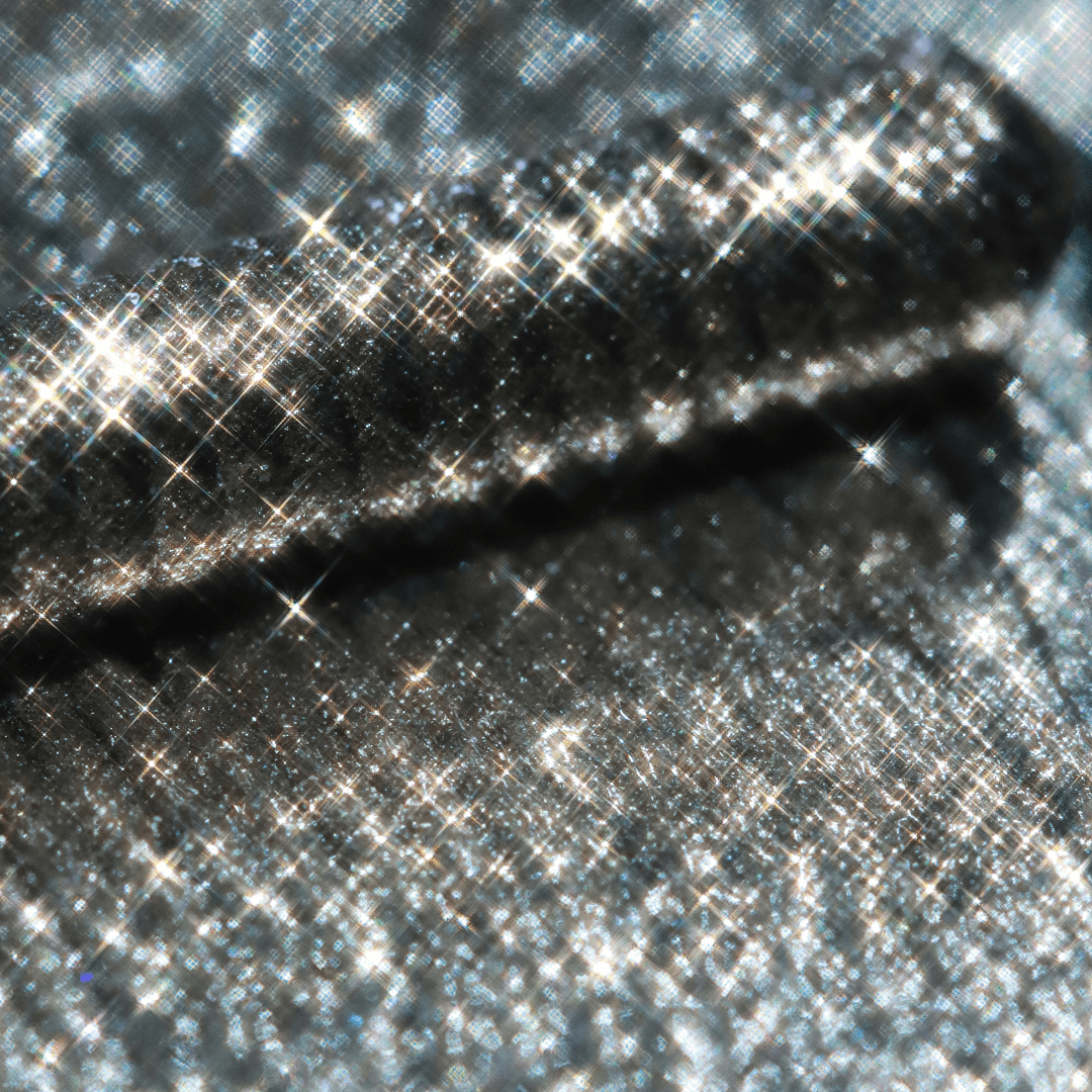 Close-up of a mascara with a shiny metallic silver finish and subtle sparkling reflections.