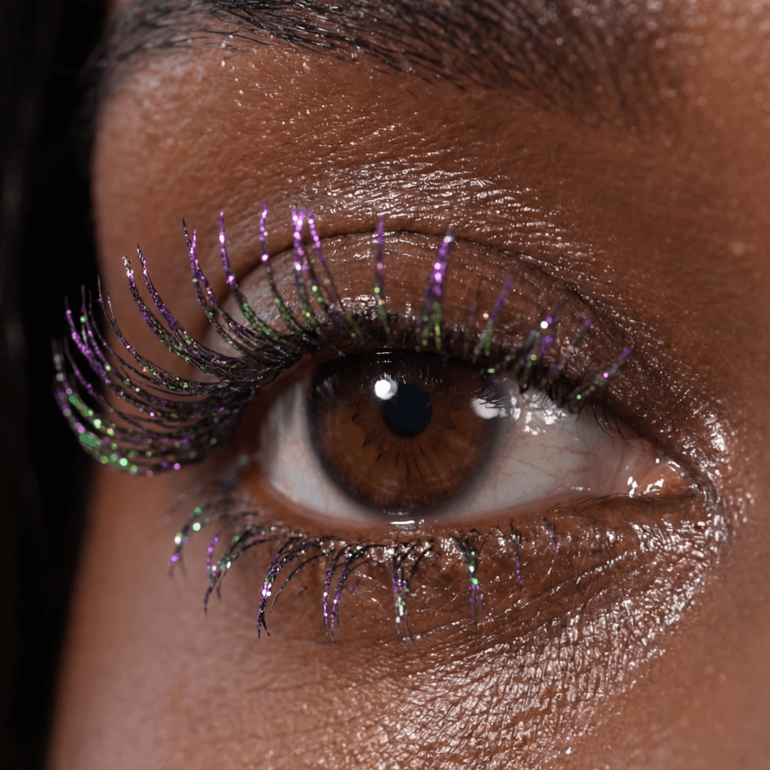 Close-up of a brown eye with visible purple and green shimmer on the lashes