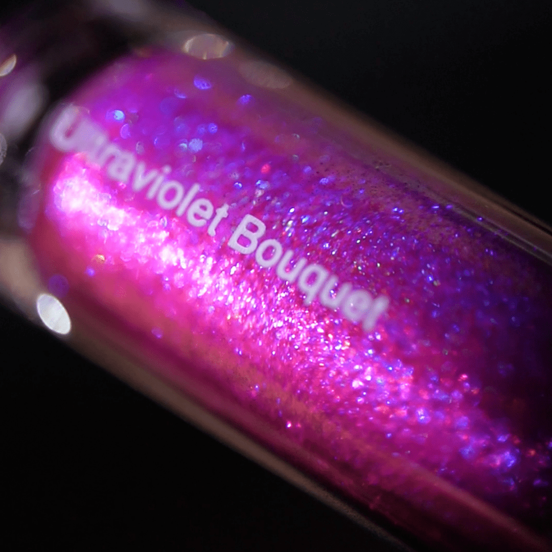 Close-up of a lip gloss tube labeled Ultraviolet Bouquet with purple and pink holographic glitter inside.