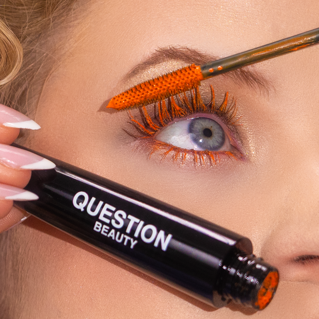 Close-up of an eye with bright orange mascara applied to the upper lashes.