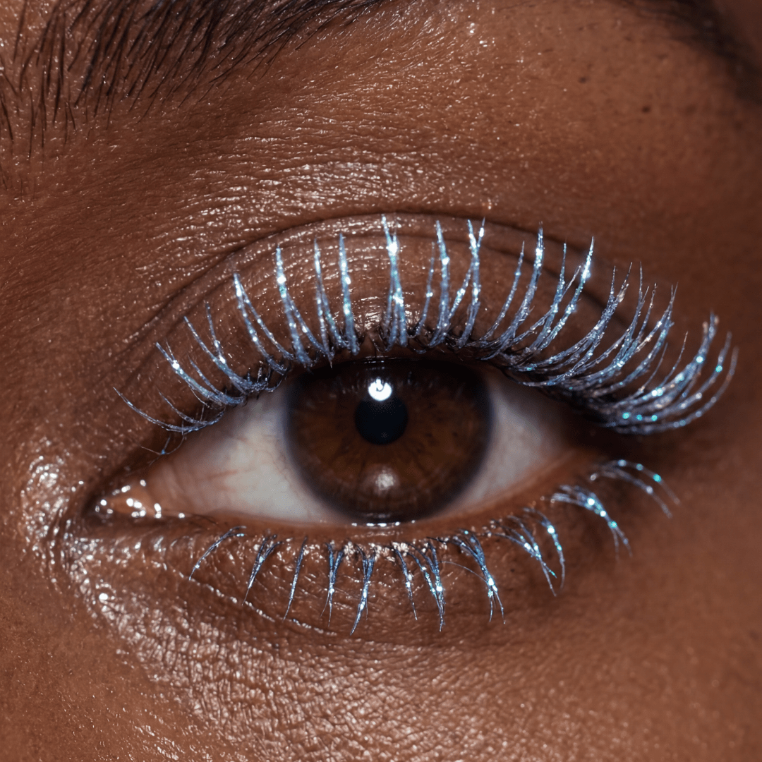 Close-up of a brown eye with frosty lilac mascara applied to both upper and lower lashes.