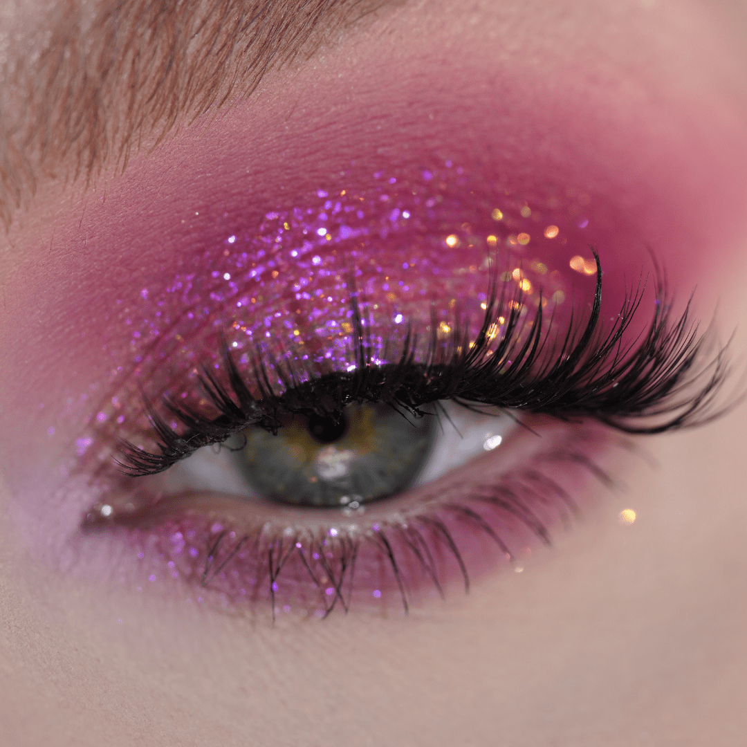 Close-up of an eye with vivid pink and purple glitter eyeshadow, long eyelashes, and iridescent shimmer.