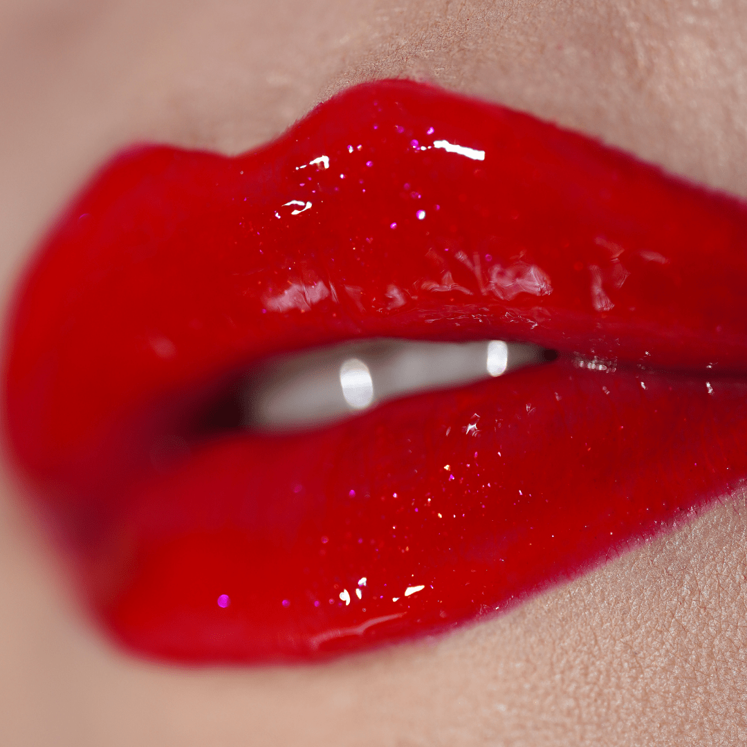 Close-up of glossy red lips slightly parted to show white teeth and a vibrant shine.