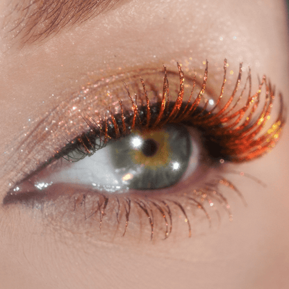 Close-up of an eye with orange-gold shimmery makeup and bold lashes