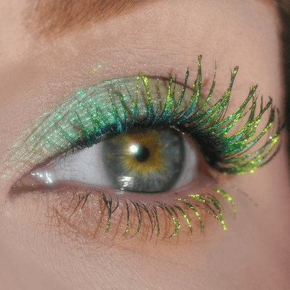 A close-up of an eye with shimmering green and yellow glitter on the eyelid and lashes