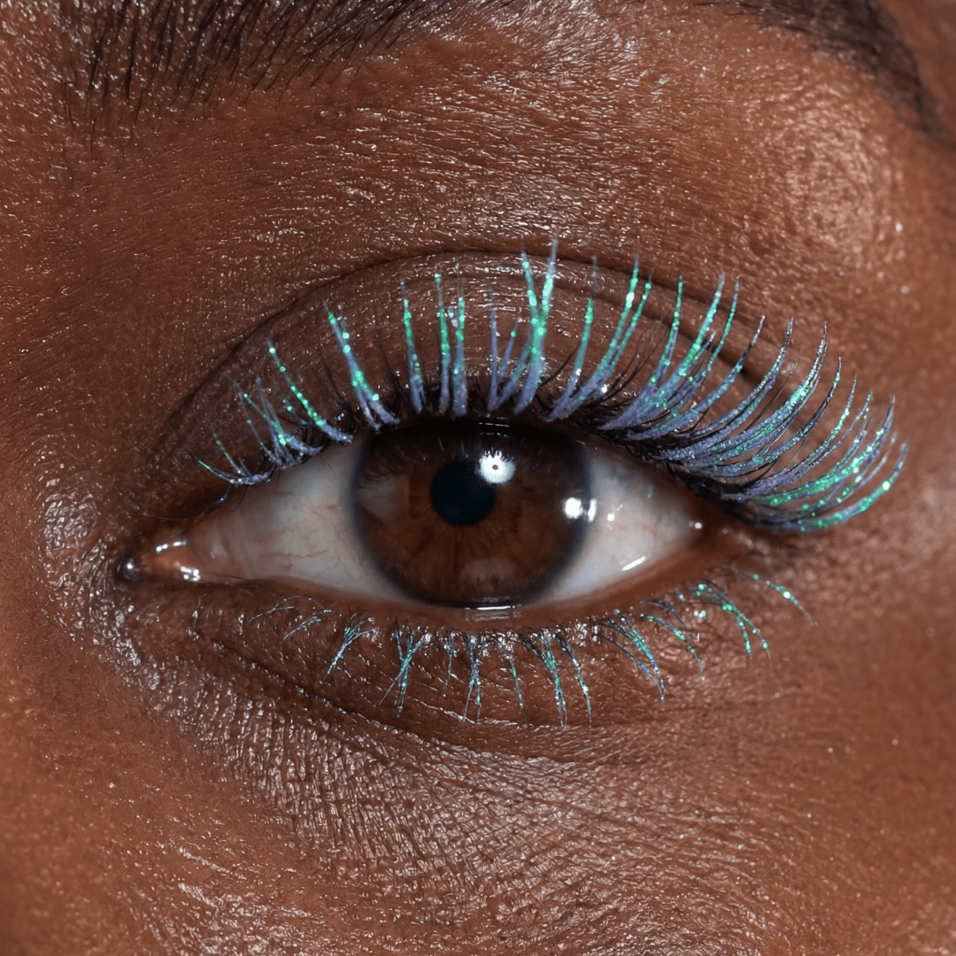 Close-up of a brown eye with long lashes coated in bright turquoise mascara.