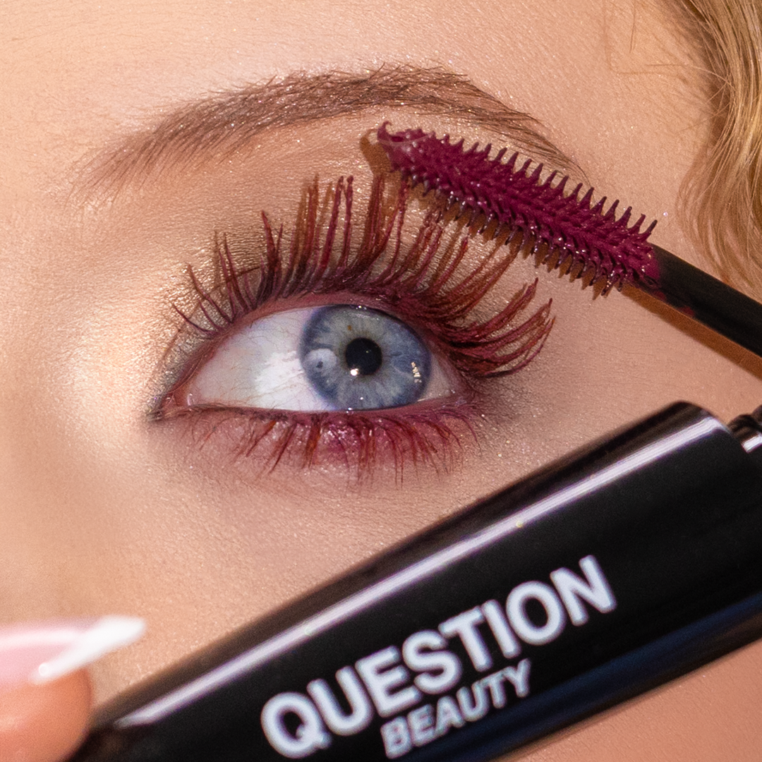Close-up of a person applying deep burgundy mascara to their upper eyelashes.