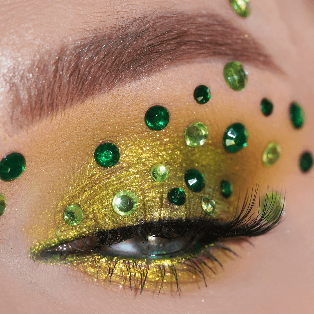 A close-up of an eye with green rhinestones and gold-green glitter eyeshadow on the eyelid.