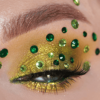 A close-up of an eye with green rhinestones and gold-green glitter eyeshadow on the eyelid.