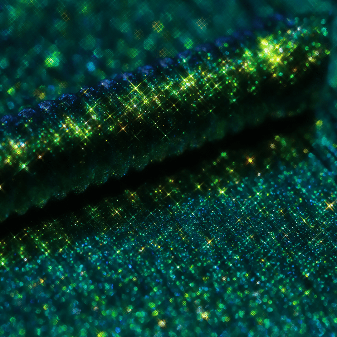 Close-up of mascara with sparkling green glitter and an iridescent, shimmering texture.