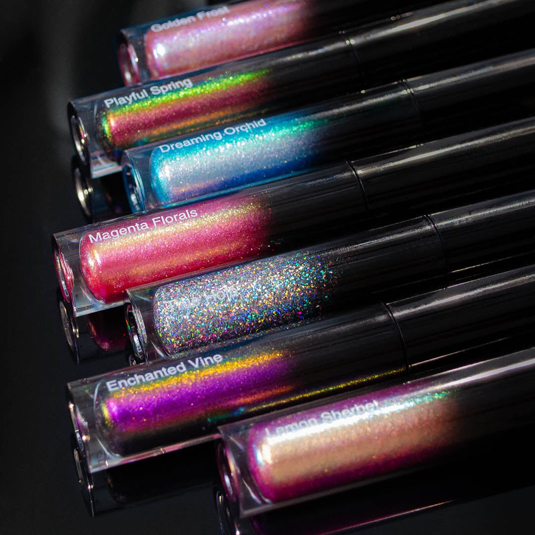Seven tubes of Lipgloss in various shimmering shades are arranged side by side.