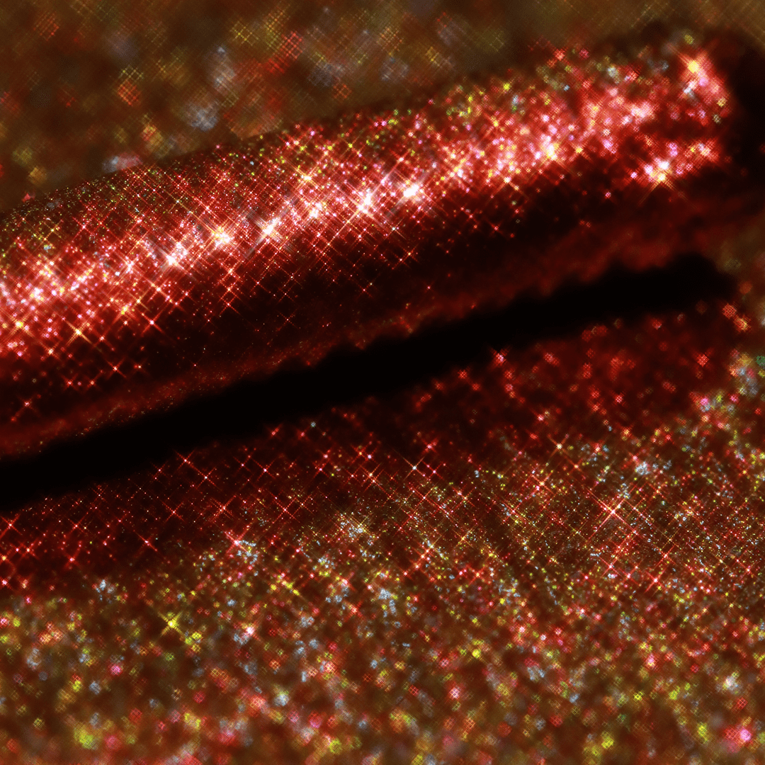 Close-up of Mascara Topper Bronze Mirage showing red and gold glitter with crosshatched reflections.
