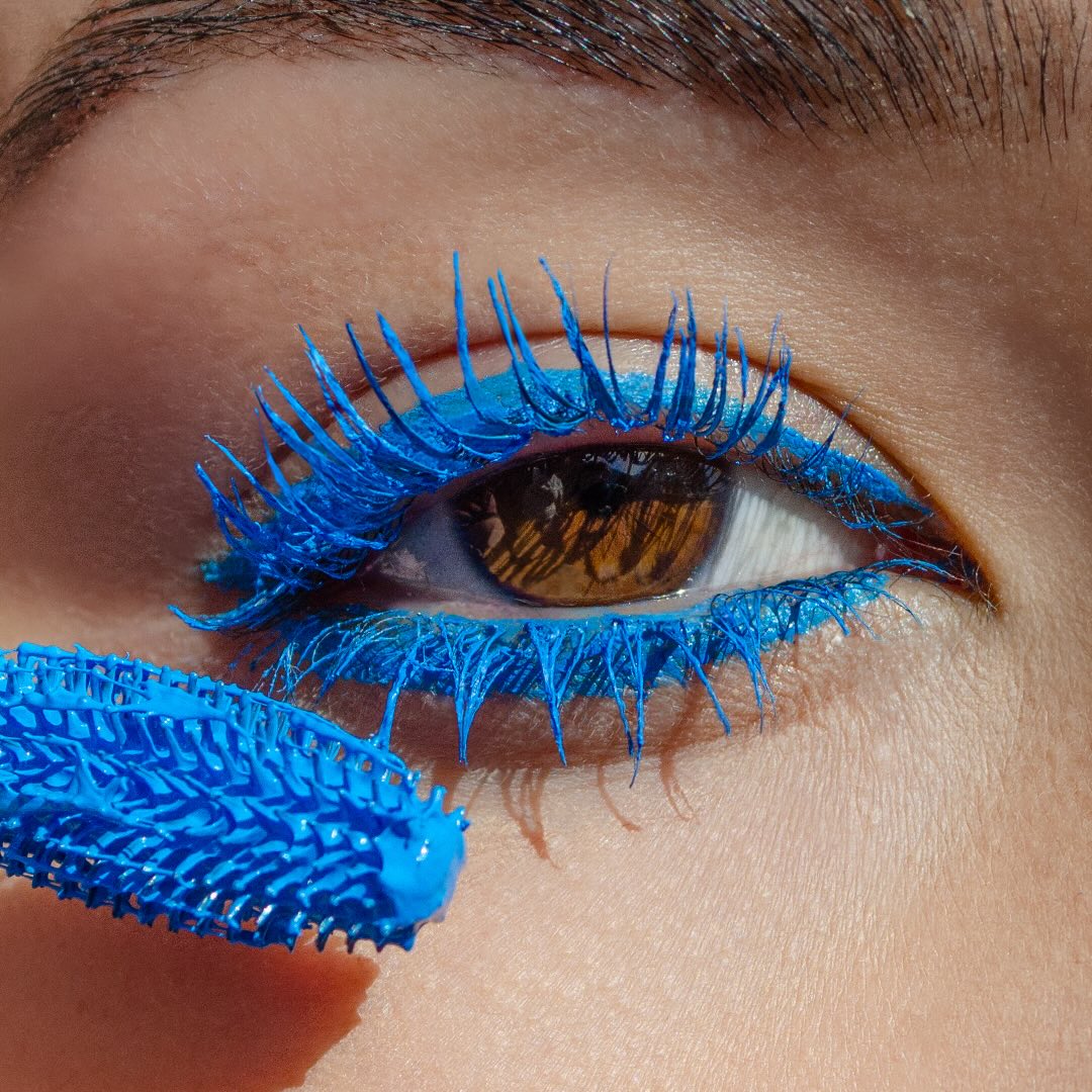 Close-up of a brown eye with blue mascara on upper and lower lashes.