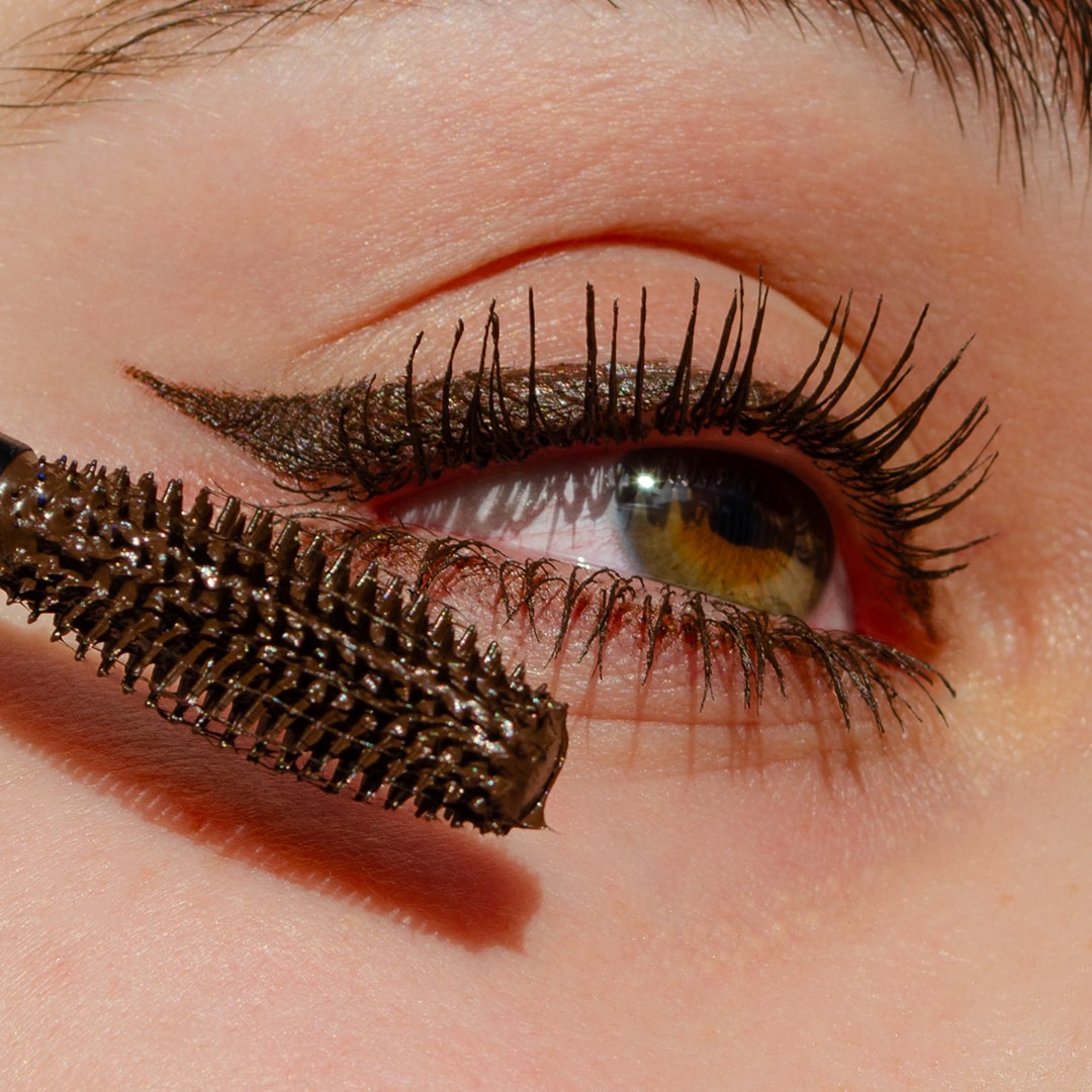 Close-up of an eye with winged liner as brown mascara is applied to the upper lashes.