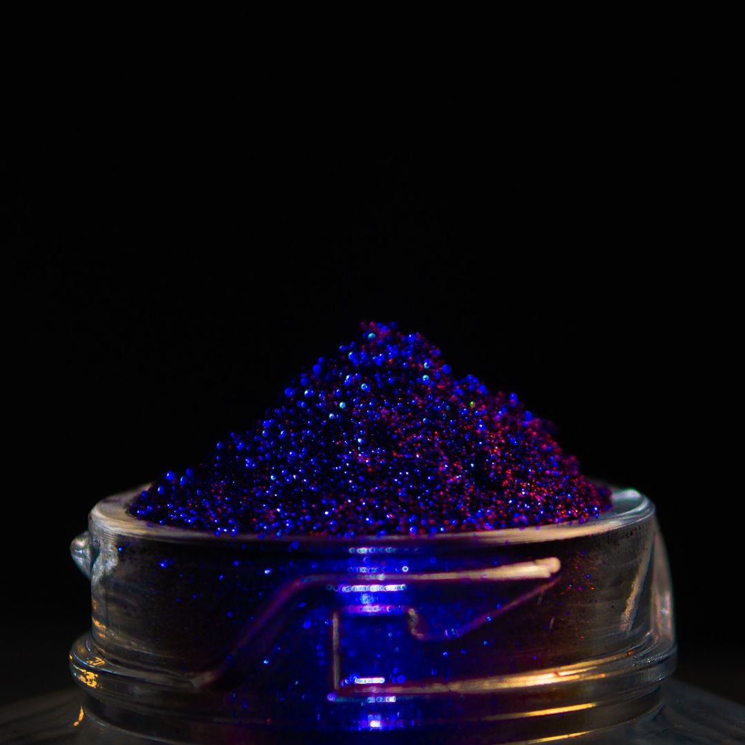 A small glass jar is filled with purple and blue glitter, shown against a black background.