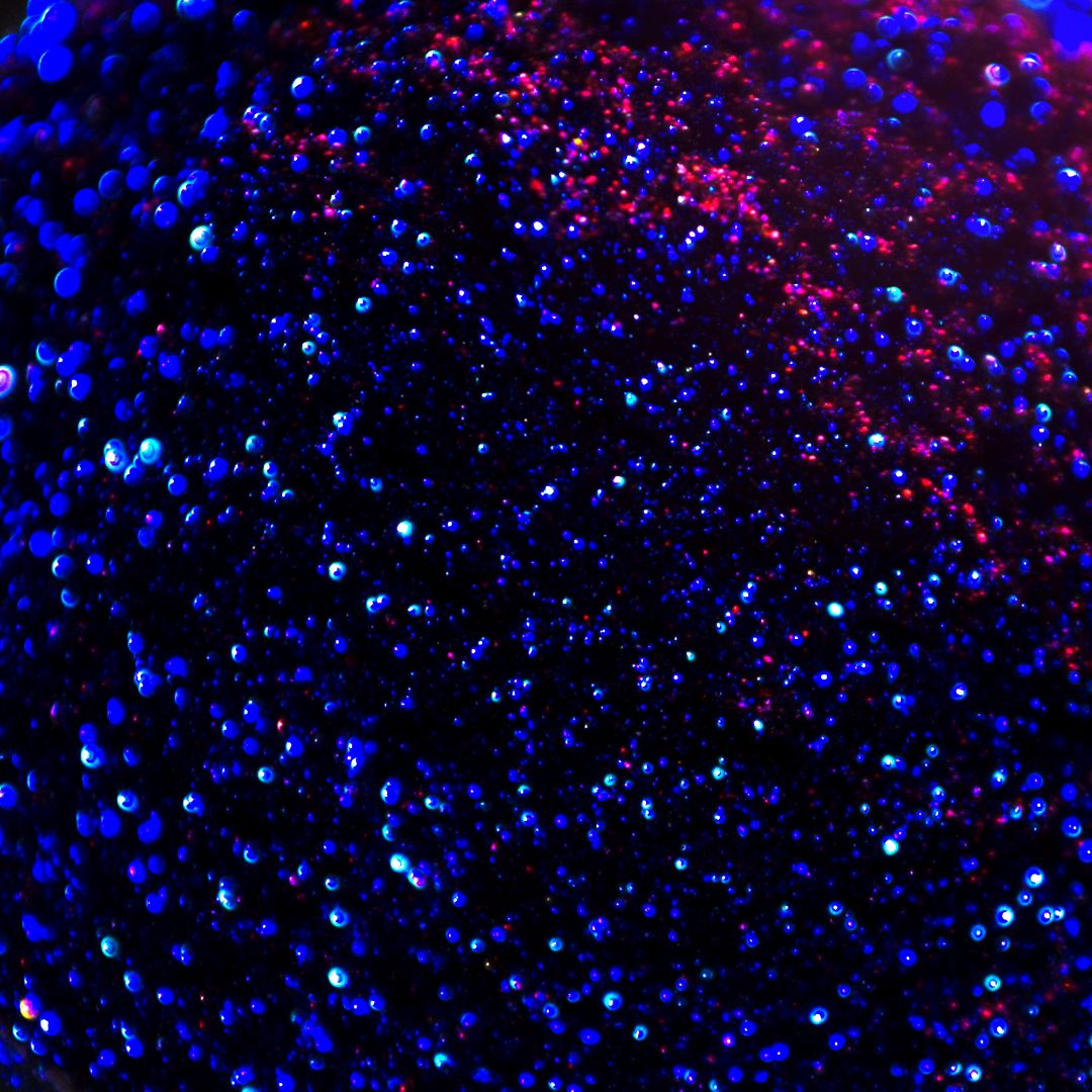 Close-up of blue holographic glitter with red and purple highlights.