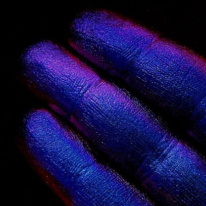 Close-up of fingertips painted in shimmering blue and purple pigment against a black background.