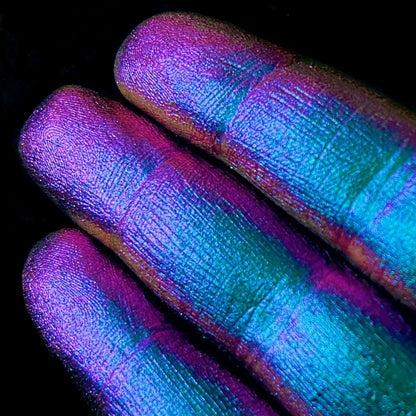 Fingers with shimmery purple blue and green pigment rest against a plain black background.