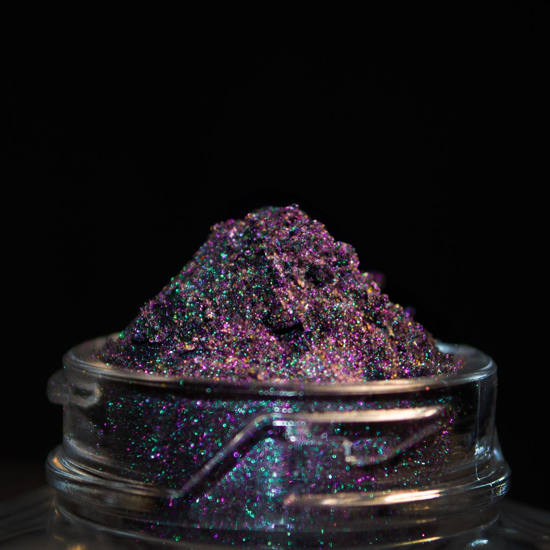 A close-up of a jar filled with holographic grey glitter sits against a black background.