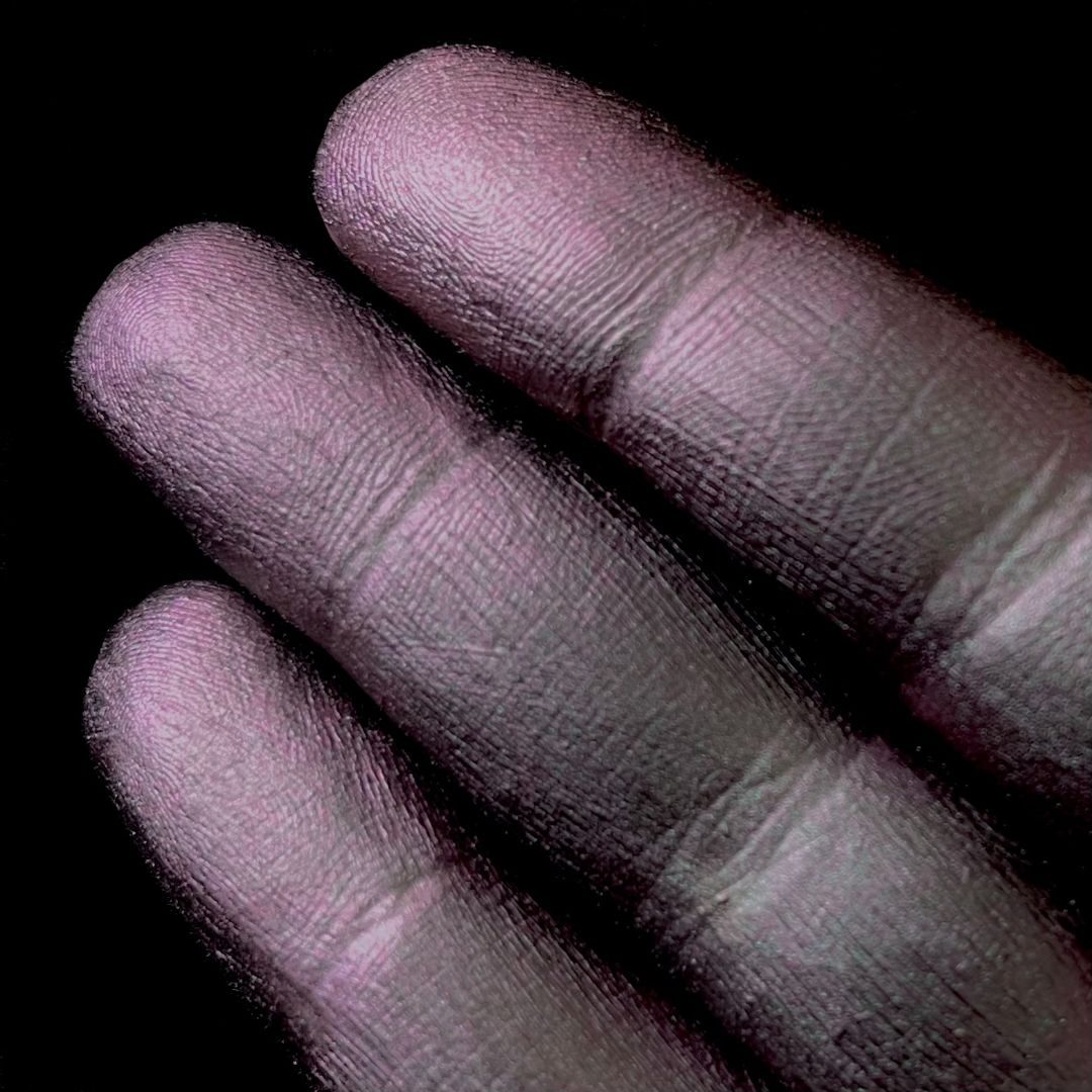 Three fingers display iridescent dark grey pigment on their nails against a solid black background.